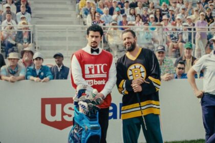 Adam Sandler as Happy Gilmore in his Boston Bruins hockey jersey, holding a golf club, standing next to his caddy on a golf course with spectators in the background.