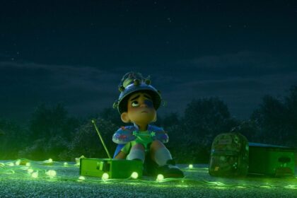 Elio, a young boy, sits on a rooftop at night surrounded by glowing green lights, looking up at the sky with a makeshift helmet, yearning for alien contact.