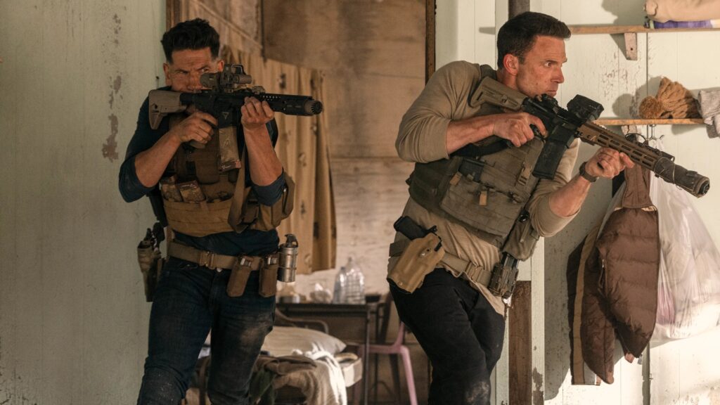 Ben Affleck as Christian Wolff and Jon Bernthal as Braxton, heavily armed and engaged in a gunfight inside a dilapidated building during The Accountant 2.